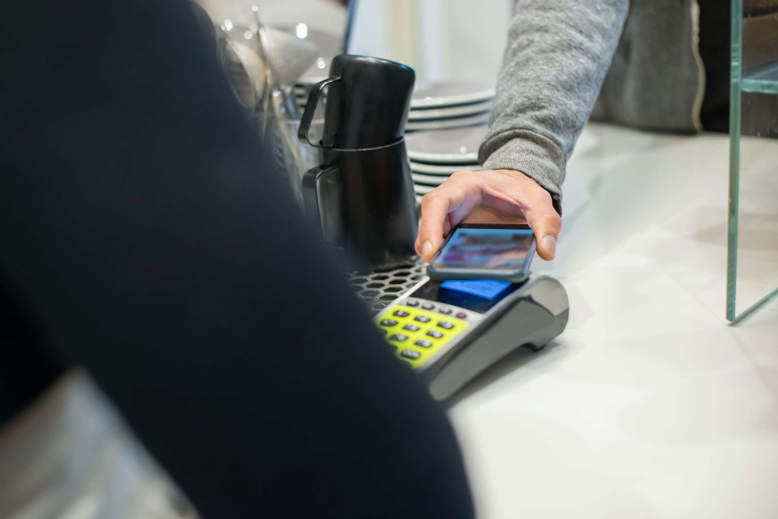 A customer makes a contactless payment using a smartphone at a café, showcasing modern digital transactions.