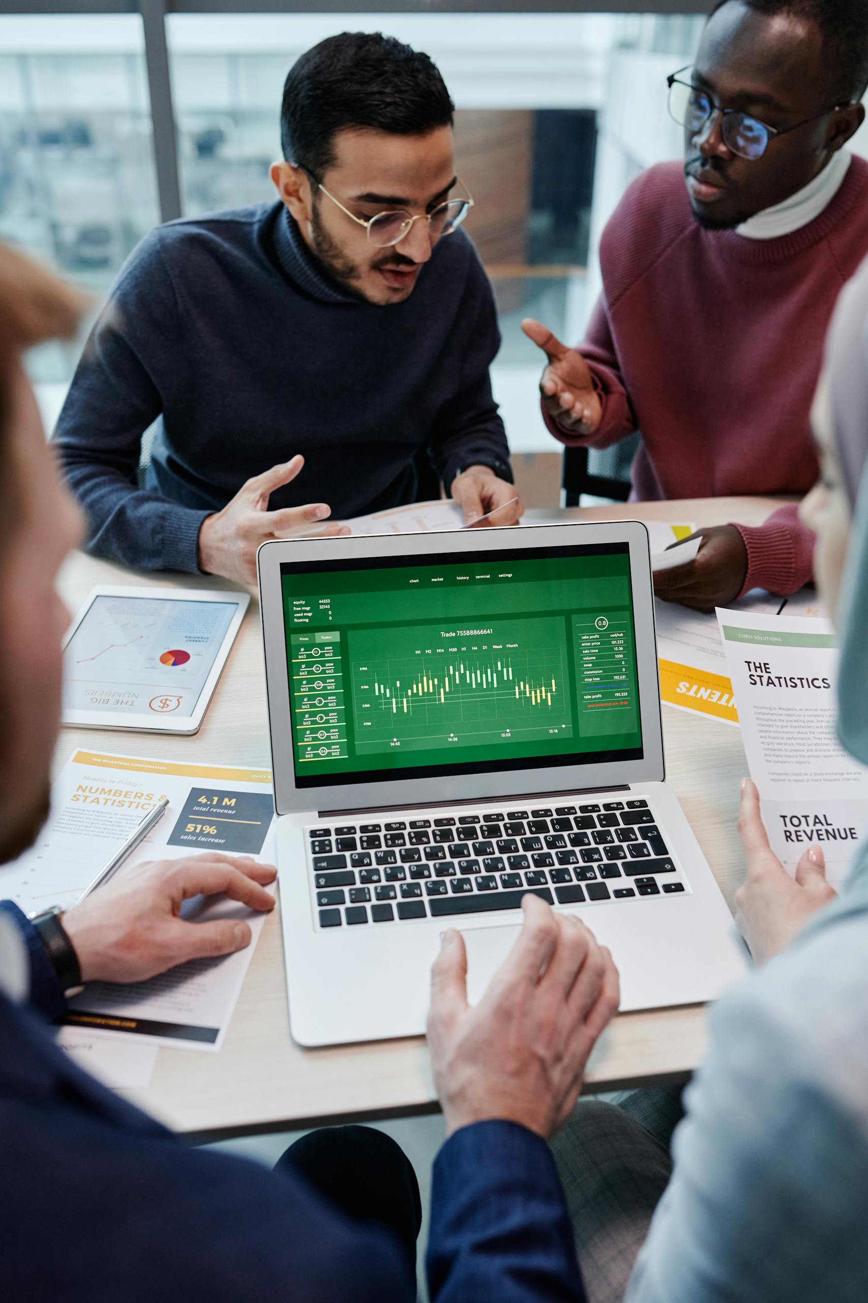 A diverse group of professionals discussing financial charts on a laptop in a modern office setting.